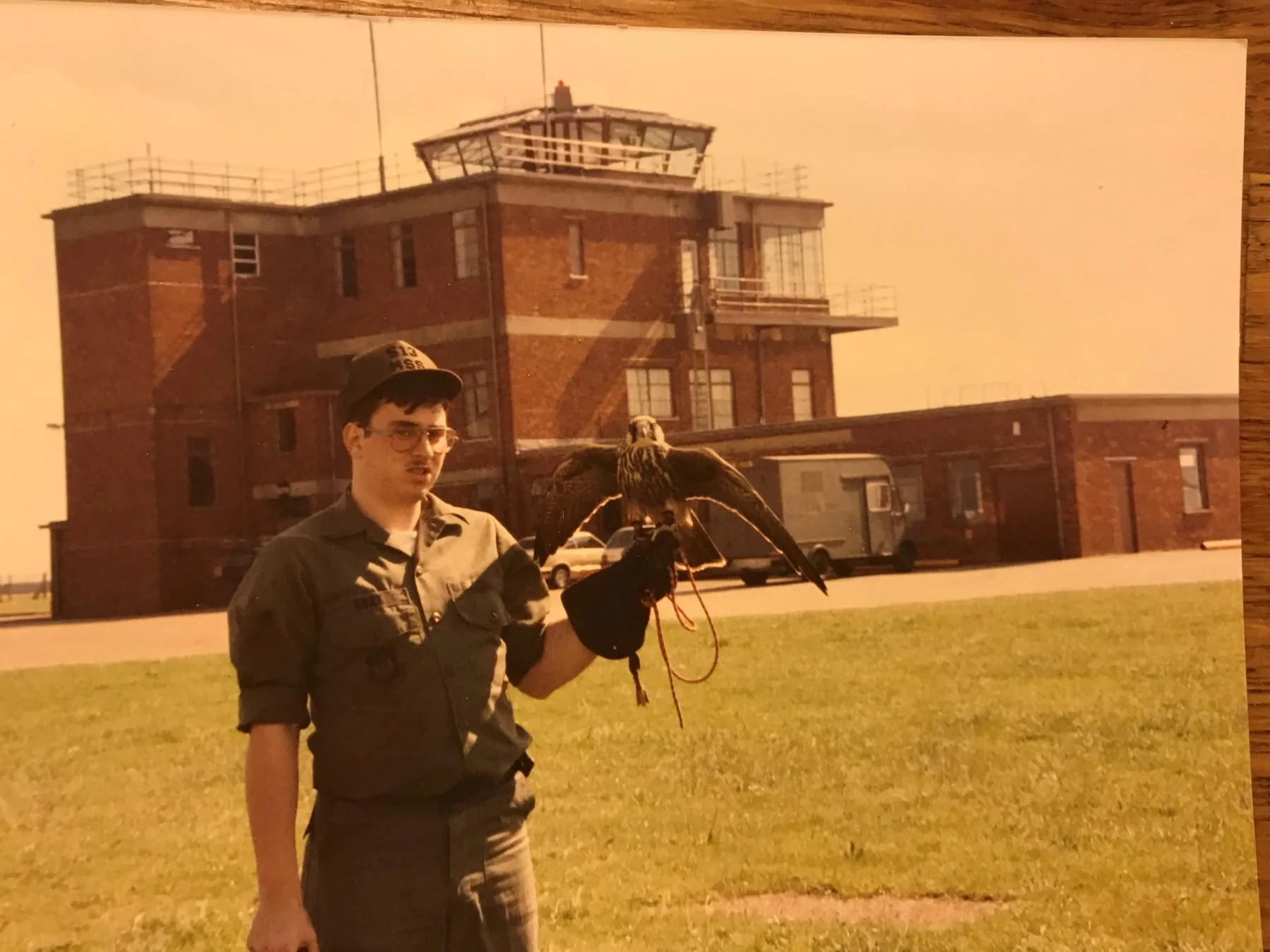 USAF airman in uniform holding an imprint peregrine falcon on the glove at RAF Lakenheath — control tower visible in the background