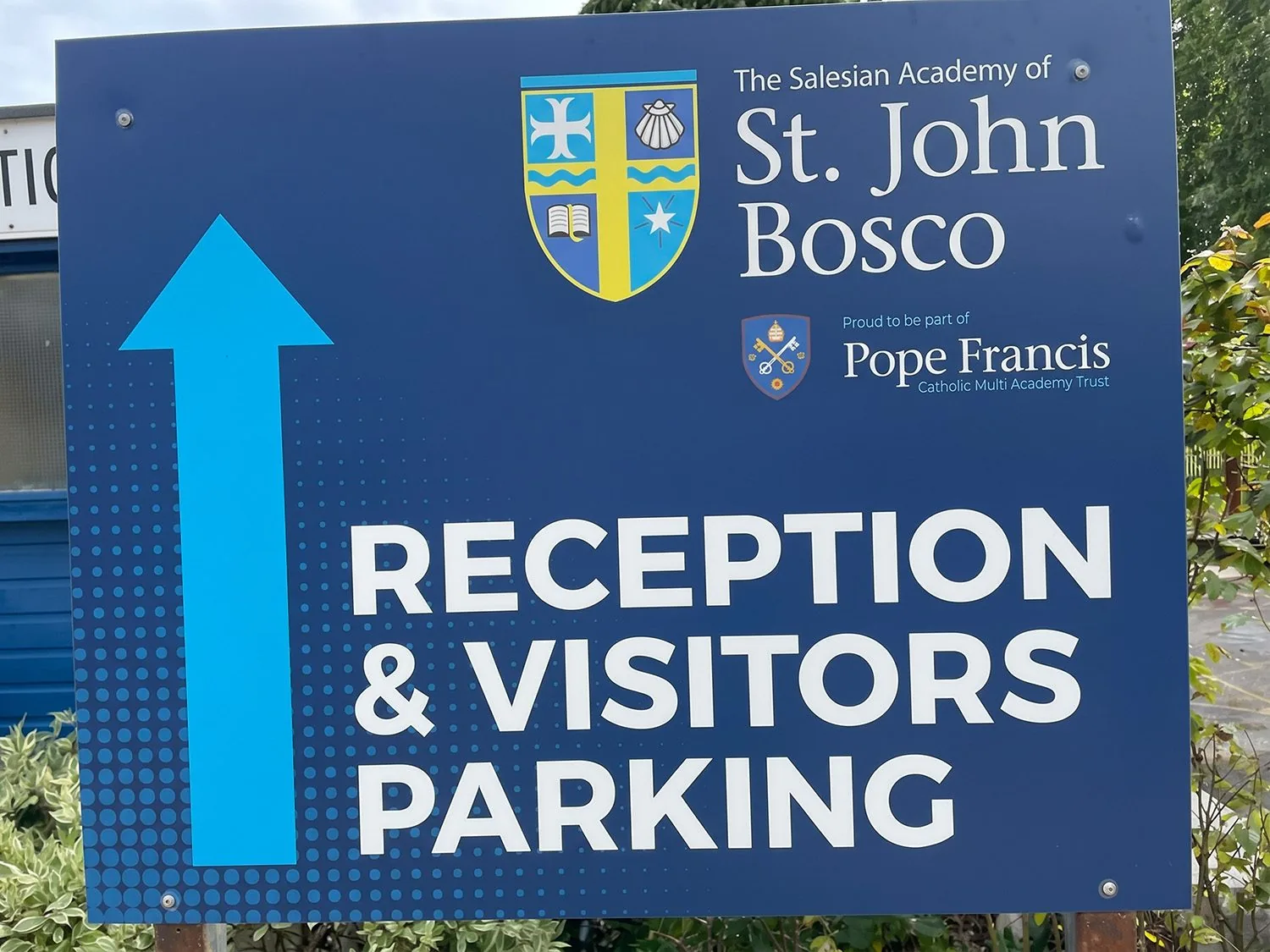 The Salesian Academy of St John Bosco school signage — blue directional sign showing school crest and Pope Francis Catholic Multi Academy Trust branding